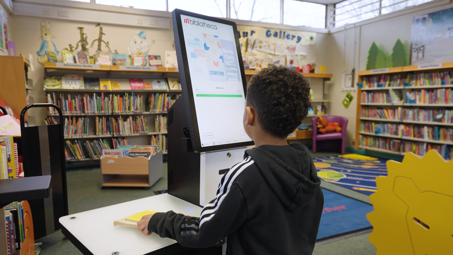 Page d’accueil 2 A child uses a Bibliotheca selfCheck 3000 kiosk in a public library, showing how modern self-service technology supports accessibility and independence.