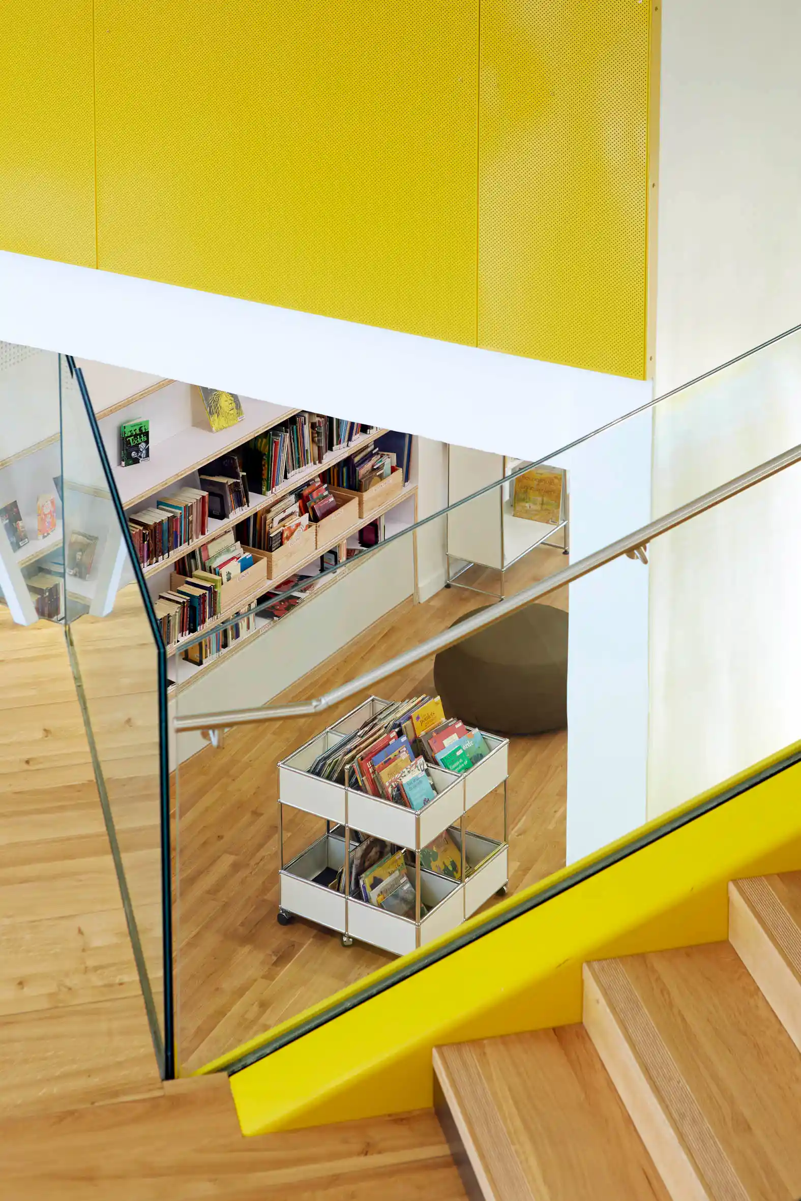 Page d’accueil 4 Vue intérieure moderne de la médiathèque B612 avec rayonnages de livres jeunesse et escalier aux finitions bois et jaune.